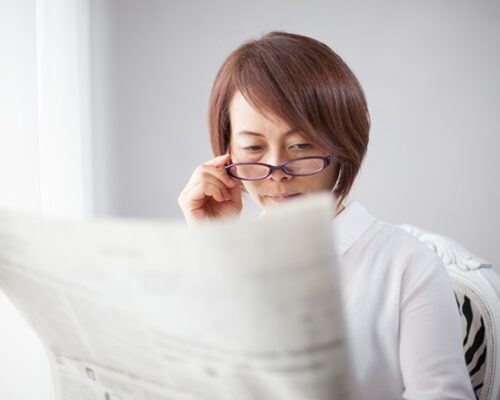 眼鏡を下ろして新聞を読む女性